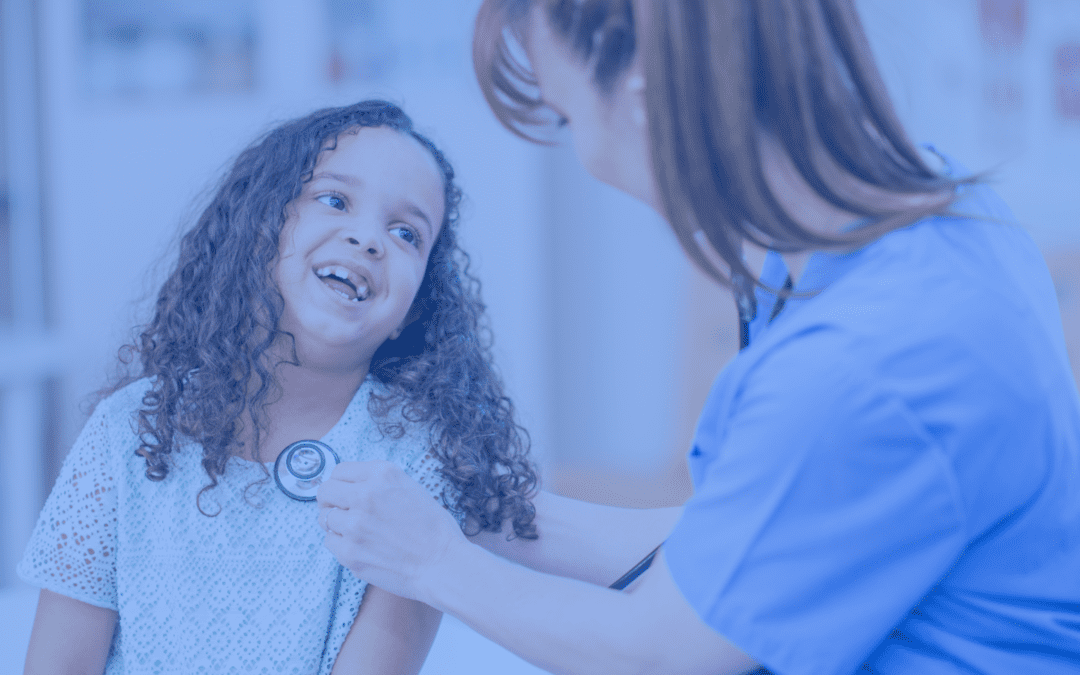 Image of a joyful young girl with curly hair, sitting at a medical clinic while a female healthcare professional listens to her heart using a stethoscope. The setting is bright and friendly, emphasizing a positive healthcare experience for children. Both individuals are smiling, highlighting a comforting and caring interaction.