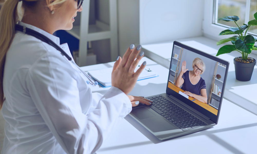 Image of a young boy in a hospital bed hugging his nurse in a comforting embrace. The nurse, wearing a light blue uniform, smiles warmly at the child, expressing care and support. They are in a brightly lit hospital room with large windows in the background, adding a serene and hopeful atmosphere to the scene.