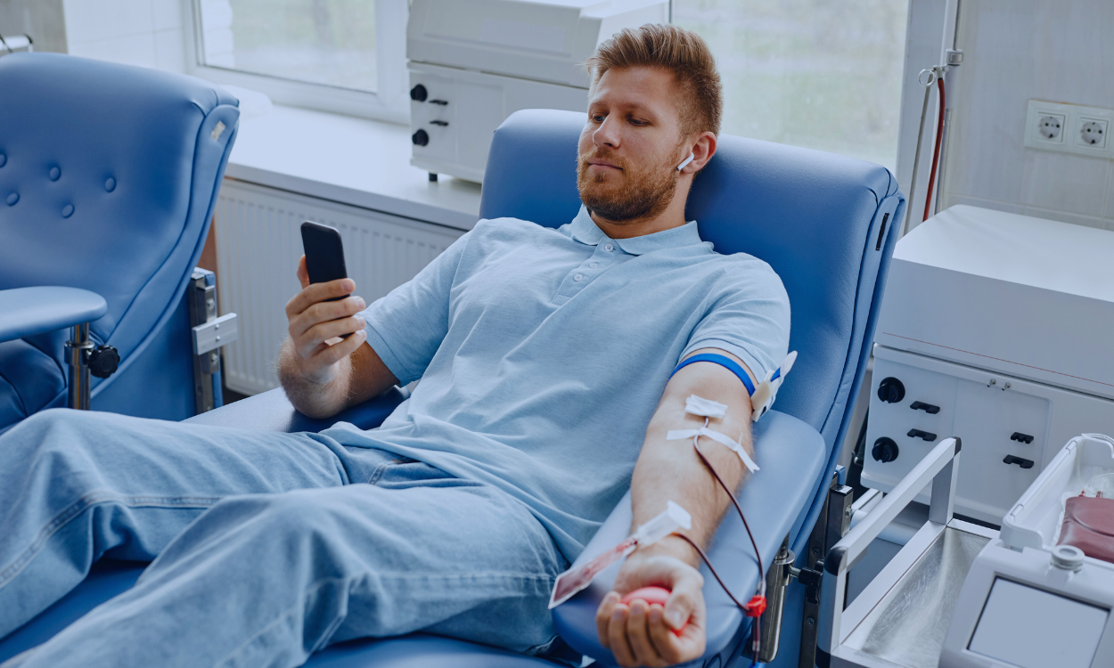 Image of a young boy in a hospital bed hugging his nurse in a comforting embrace. The nurse, wearing a light blue uniform, smiles warmly at the child, expressing care and support. They are in a brightly lit hospital room with large windows in the background, adding a serene and hopeful atmosphere to the scene.