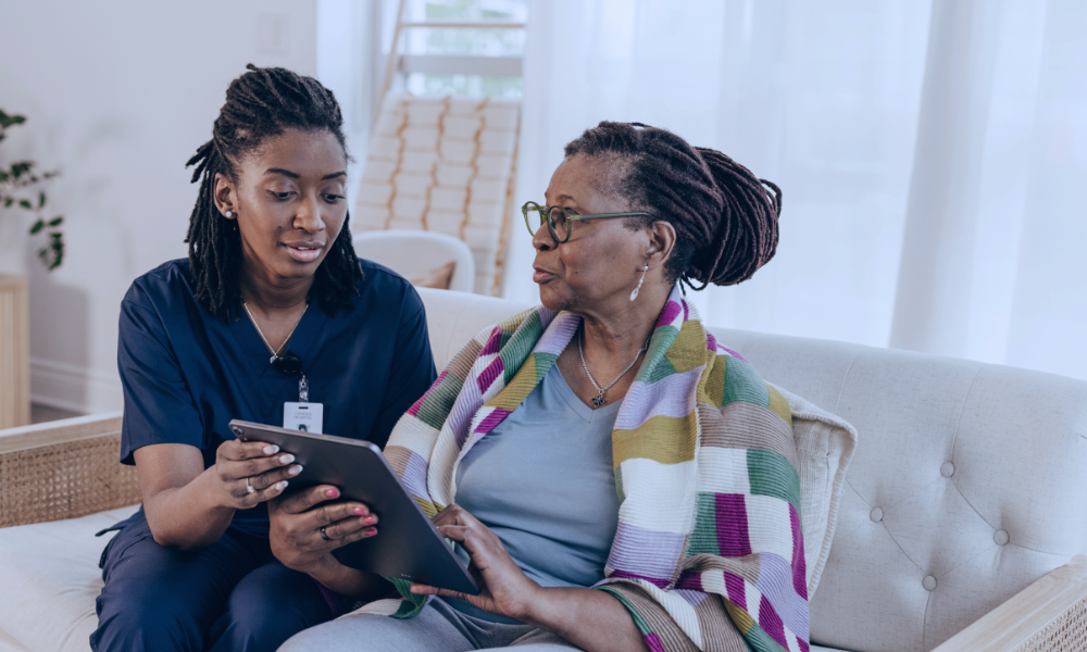 Image of a young boy in a hospital bed hugging his nurse in a comforting embrace. The nurse, wearing a light blue uniform, smiles warmly at the child, expressing care and support. They are in a brightly lit hospital room with large windows in the background, adding a serene and hopeful atmosphere to the scene.